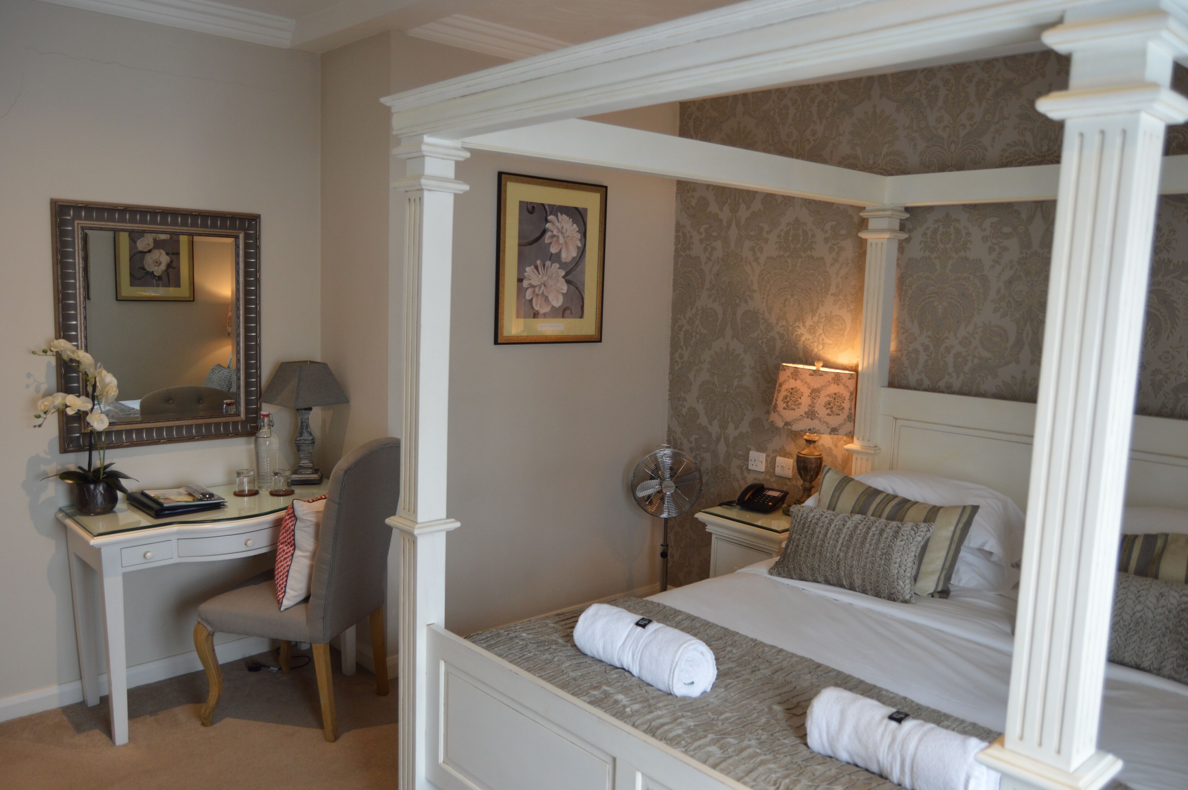 A four-poster bed with a white canopy, a desk with a chair, a mirror, and a wall-mounted lamp.