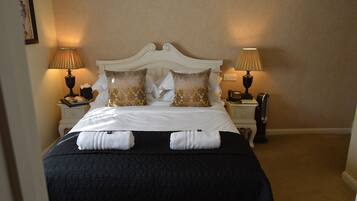 Una cama bien hecha con cabecera blanca, dos almohadas y dos toallas sobre la cama. Hay dos mesitas de noche, cada una con una lámpara y un teléfono.