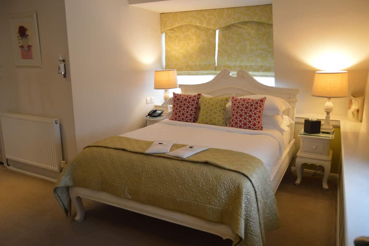 Habitación de hotel con una cama grande, dos mesitas de noche, un radiador y una ventana con cortinas.