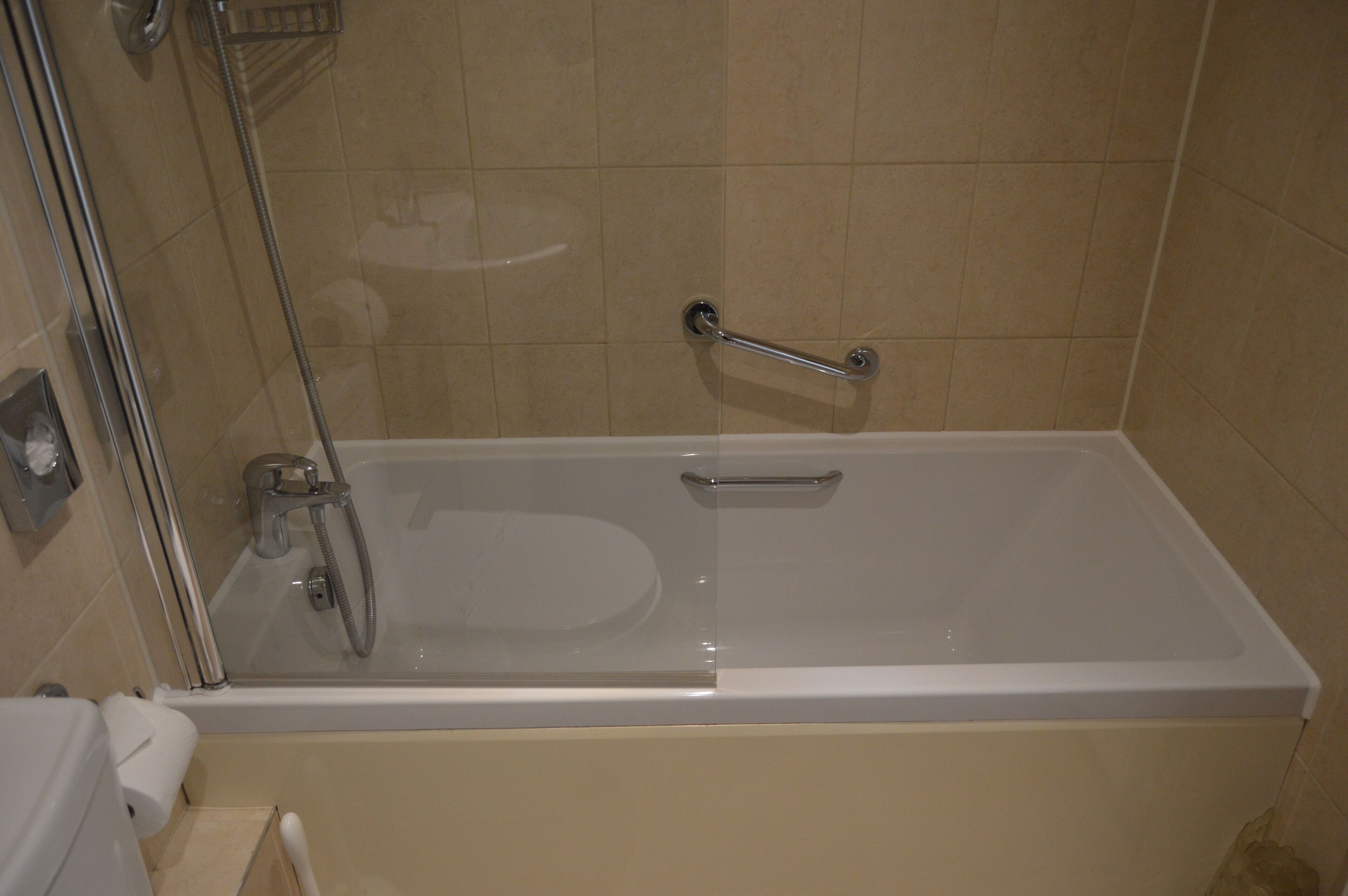 A bathroom with a bathtub, a glass shower enclosure, and a handrail.