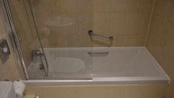 A bathroom with a bathtub, a glass shower enclosure, and a handrail.