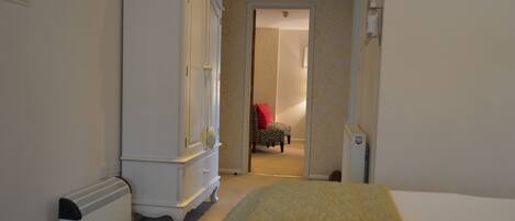 Une chambre d’hôtel avec un lit, une commode, un radiateur et une chaise au fond de la pièce.