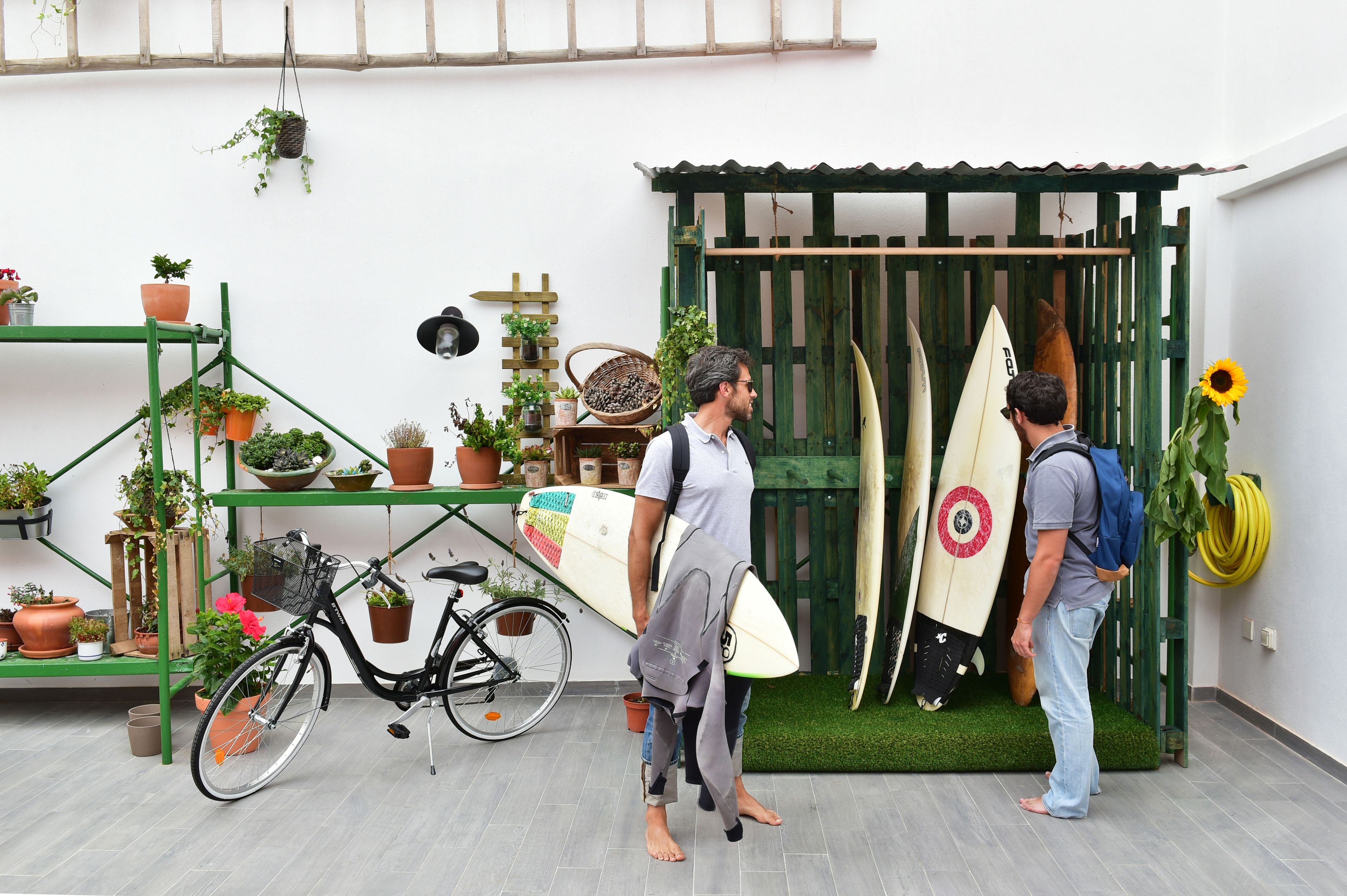 Een man houdt een surfplank vast, naast een andere man met een surfplank die tegen een houten constructie leunt.