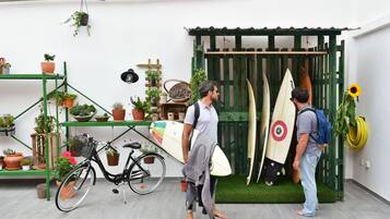 Een man houdt een surfplank vast, naast een andere man met een surfplank die tegen een houten constructie leunt.