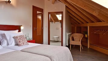 A bedroom with a wooden ceiling, a bed with patterned bedding, a red bedside table, and a chair.