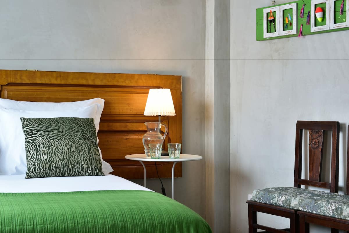 Un lit bien fait, recouvert d’une couverture verte, avec une tête de lit en bois et une lampe posée sur une petite table à côté.