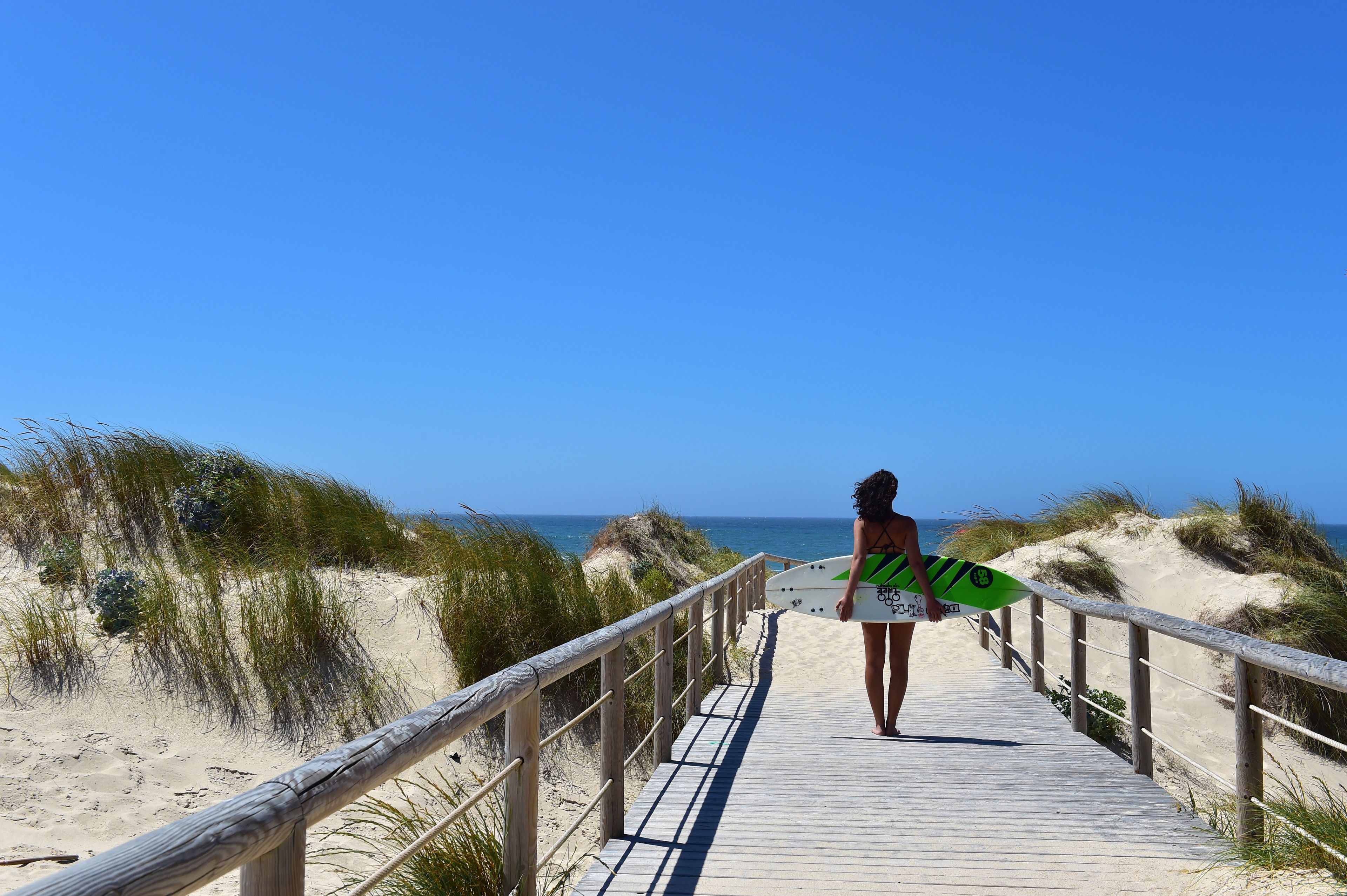 Une promenade en bois qui mène à une plage bordée de dunes de sable, avec l’océan en toile de fond.