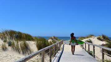 A wooden boardwalk leading to a beach with sand dunes and the ocean in the background.
