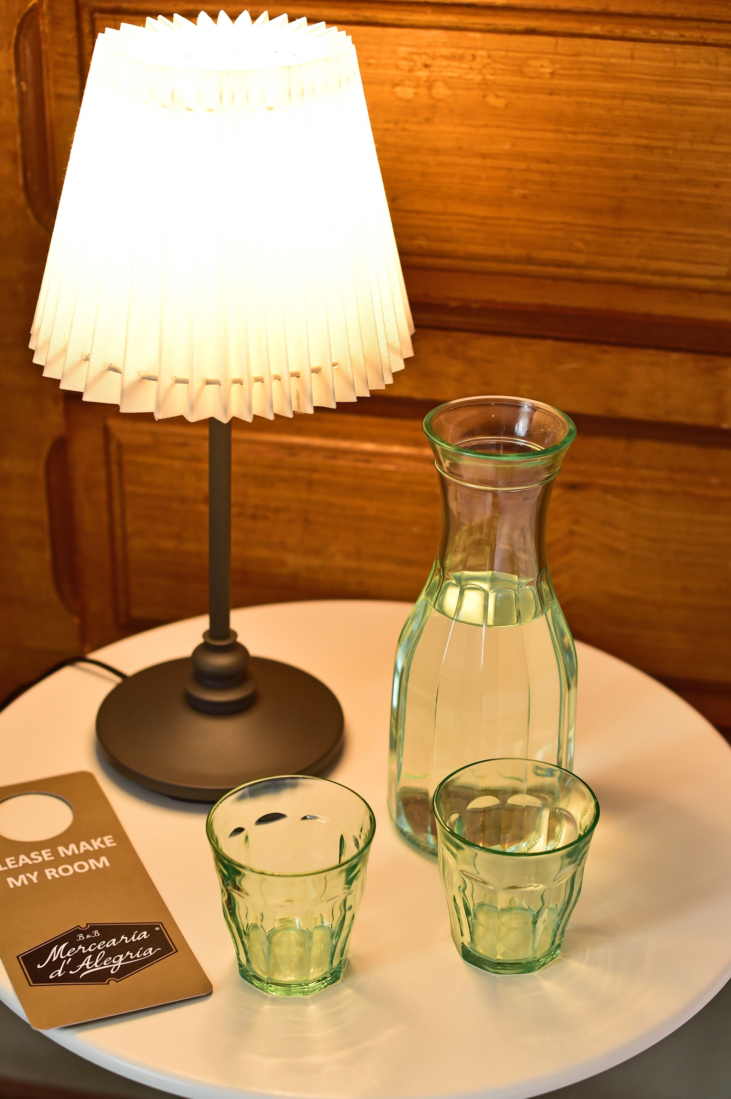 Ett bord med en lampa, en glaskaraff och två små glas.