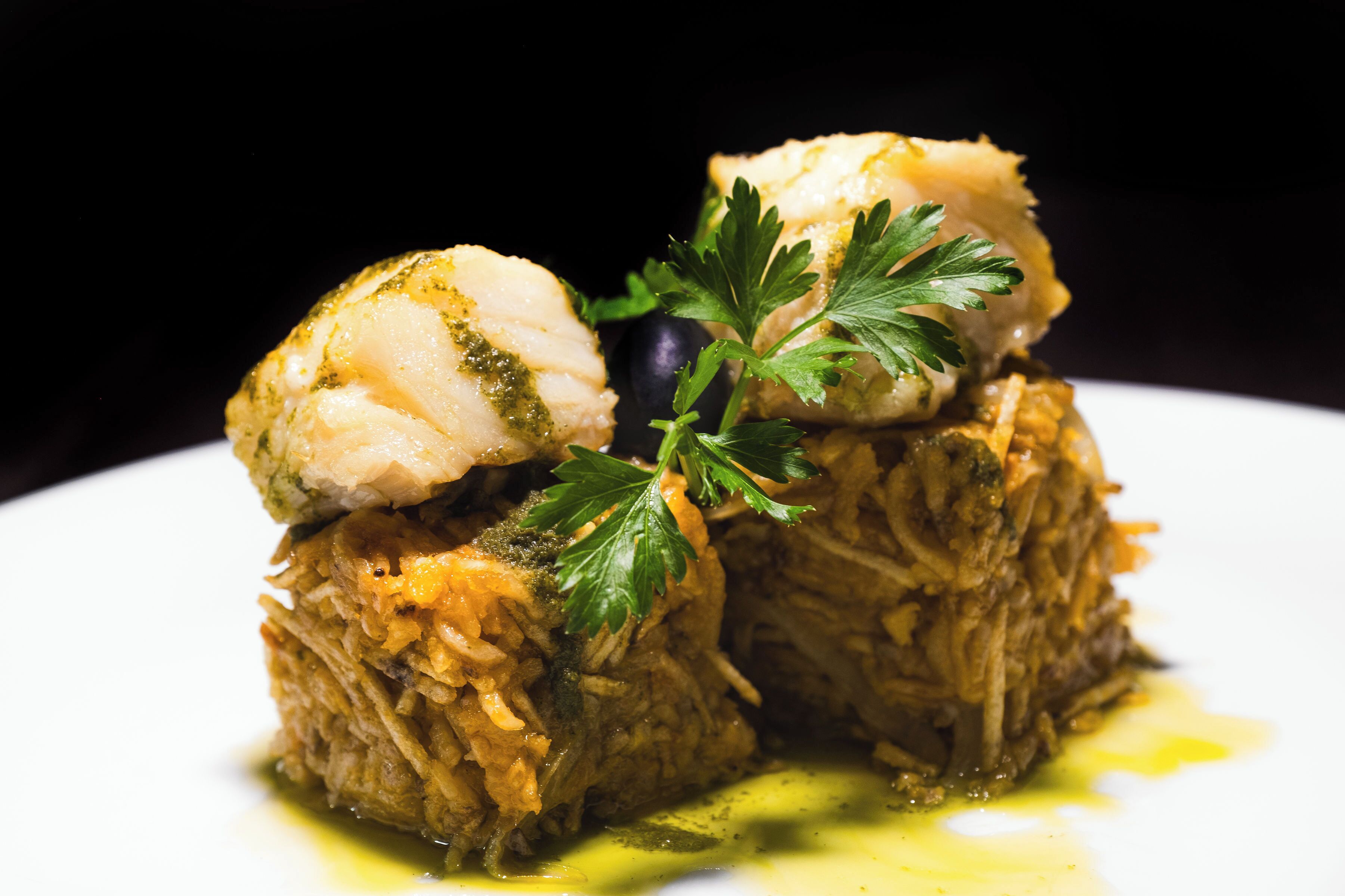 Un piatto con pesce e carne sfilacciata, guarnito con prezzemolo, su un piatto bianco.