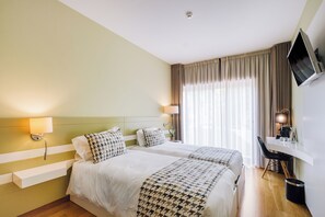 Camera d'albergo con due letti, una scrivania, una TV e una finestra con tende.