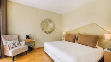 Quarto de hotel com uma cama grande, uma cadeira, mesa de cabeceira, abajur e espelho fixado na parede.