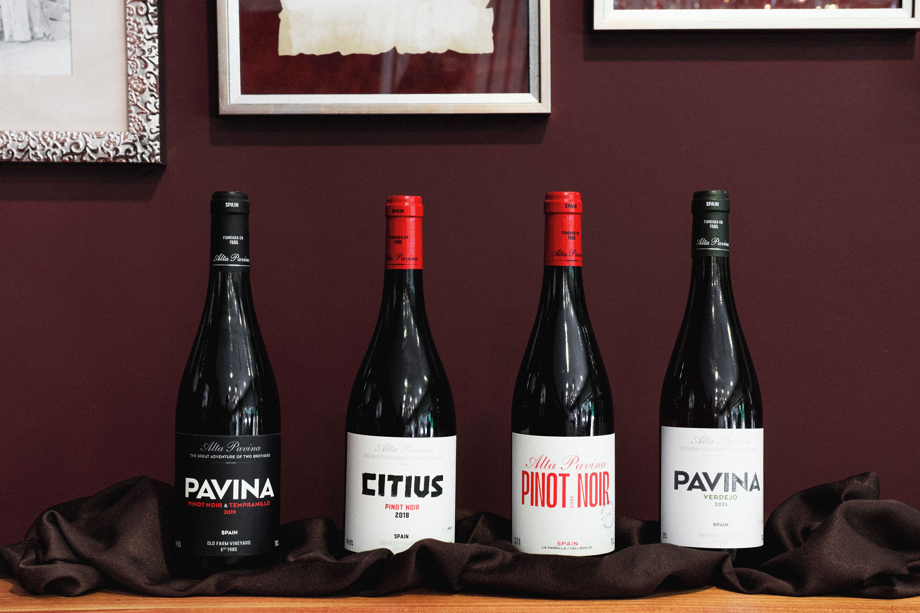 Four wine bottles on a wooden surface with a dark cloth underneath.