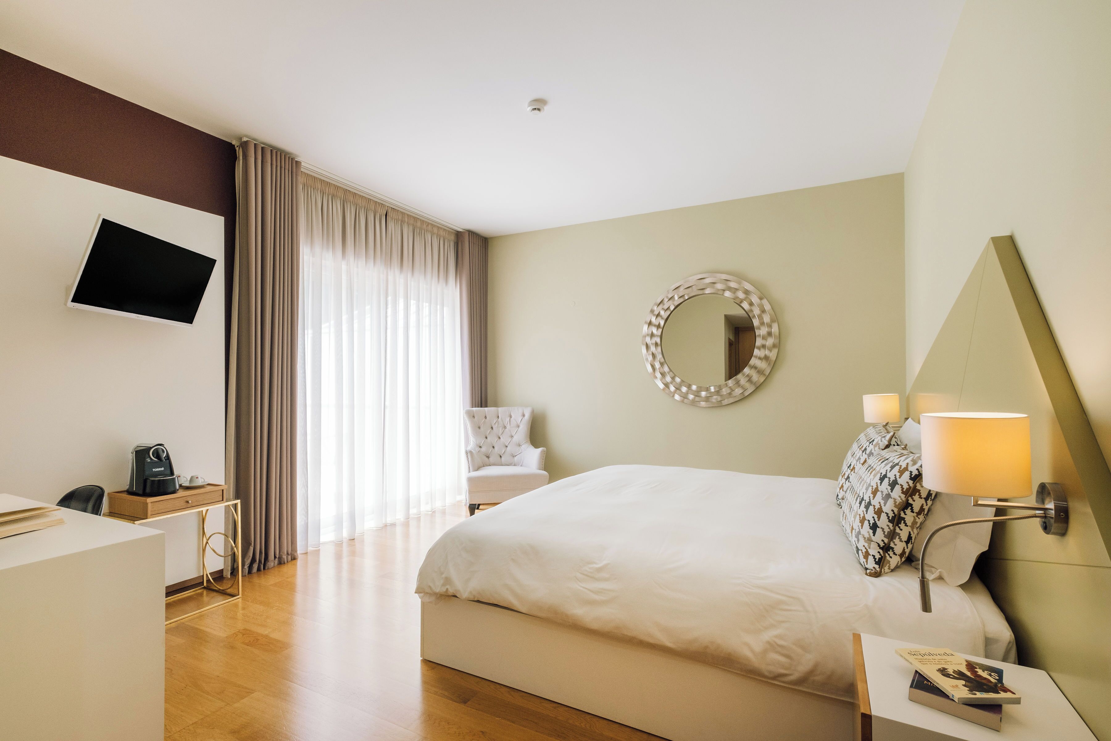 Ein Hotelzimmer mit Bett, Schreibtisch, Stuhl, Fernseher, Spiegel und Lampe.