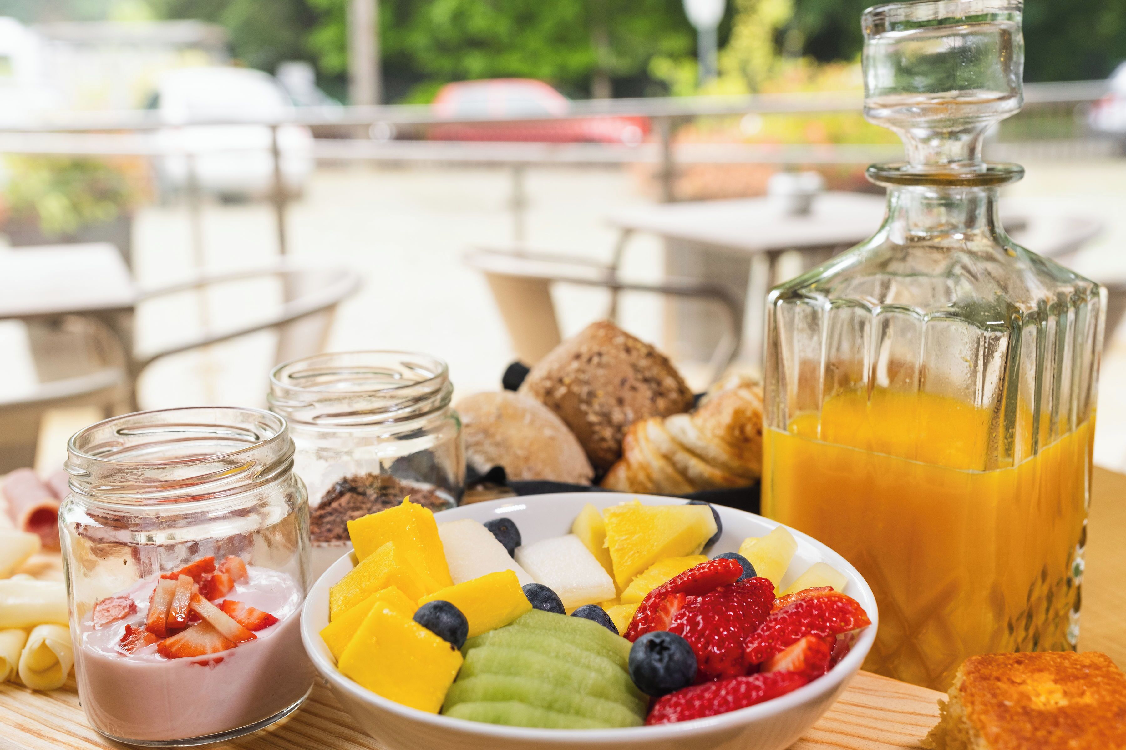 A breakfast setting with a bowl of fruit, a glass of orange juice, and a jar of yogurt parfait.