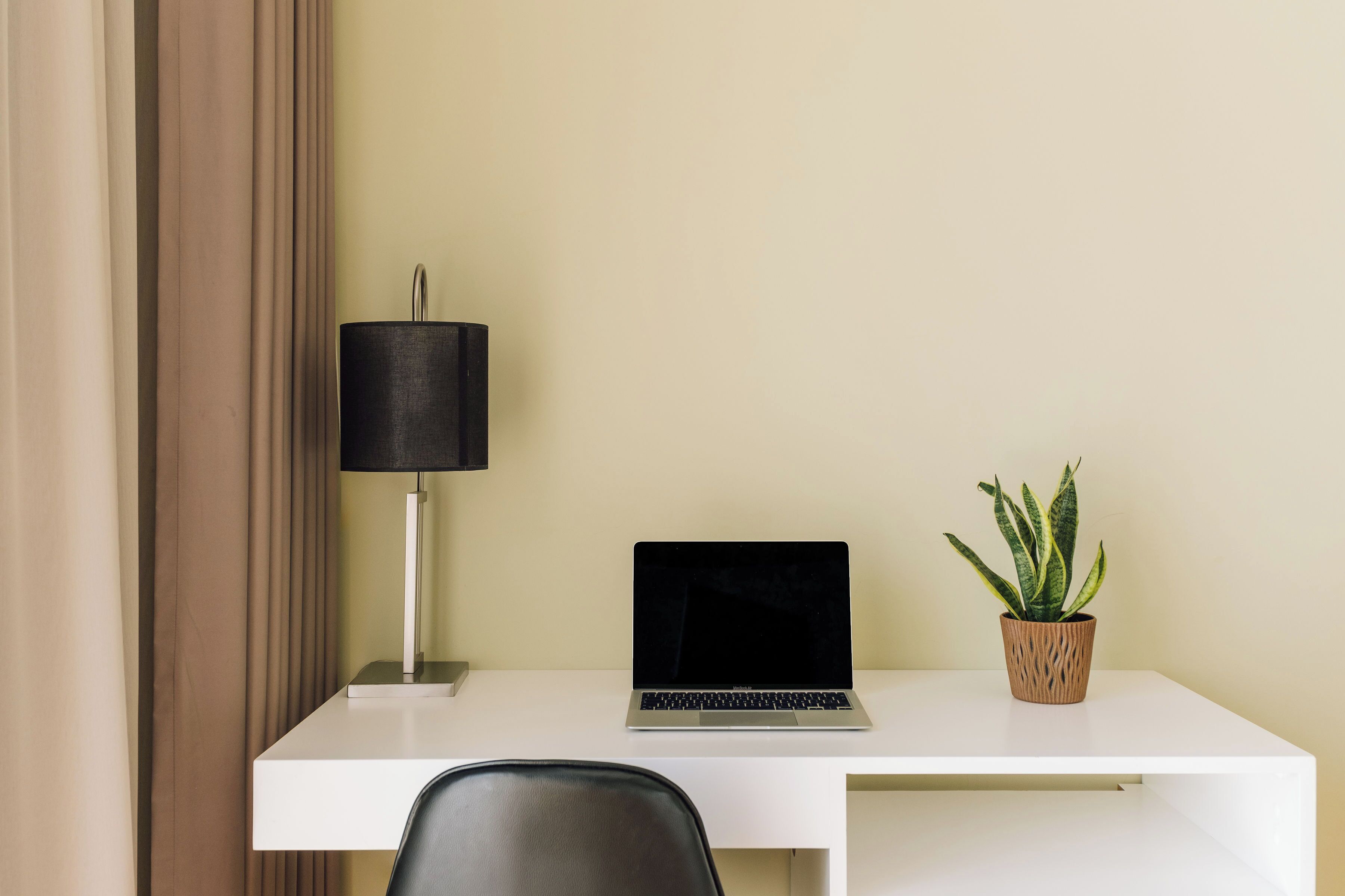 Un bureau blanc avec un ordinateur portable, une lampe noire et une plante en pot.