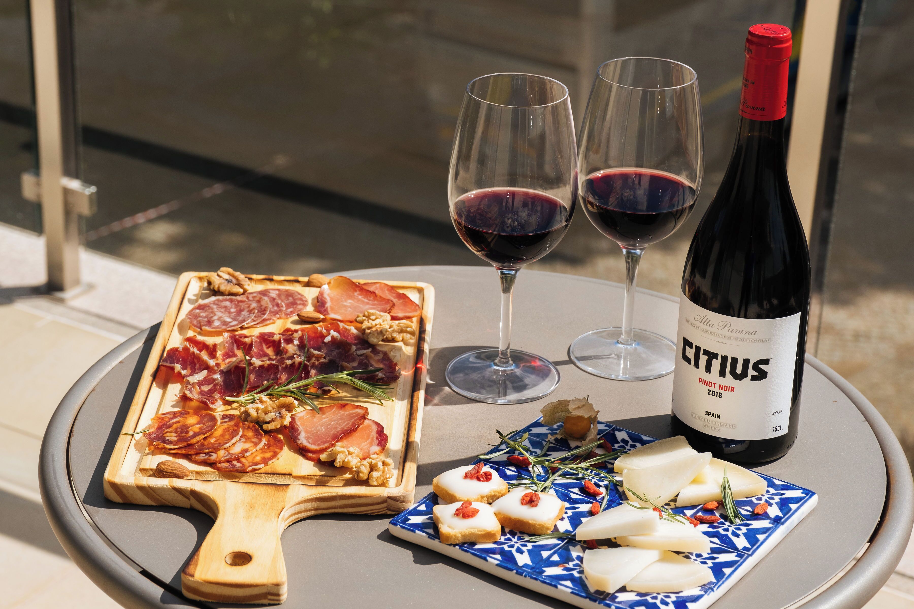 Una mesa con una tabla de embutidos, dos copas de vino tinto y una botella de Citius Pinot Noir 2018.