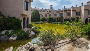 A courtyard with a pond, surrounded by buildings with arched doorways and a tower. - Apartamentos Turísticos Bahía Sur (San Fernando)