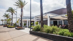 A modern building with a covered outdoor seating area, palm trees, and a clear sky. - Apartamentos Turísticos Bahía Sur (San Fernando)