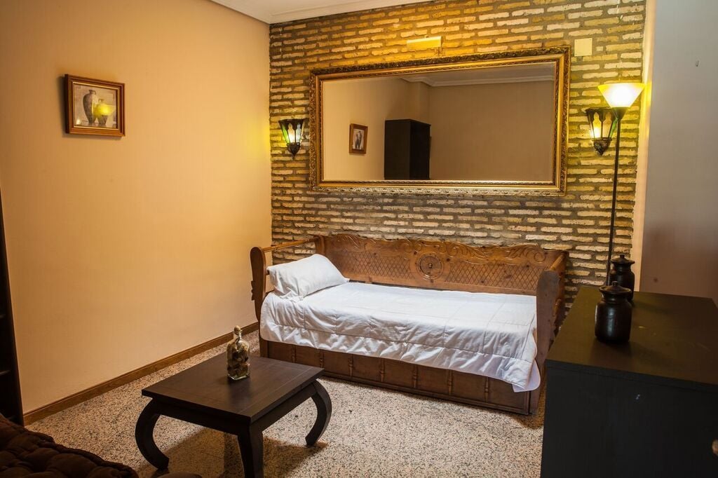 A room with a brick wall, a large mirror, a wooden sofa, a small table, and a lamp.