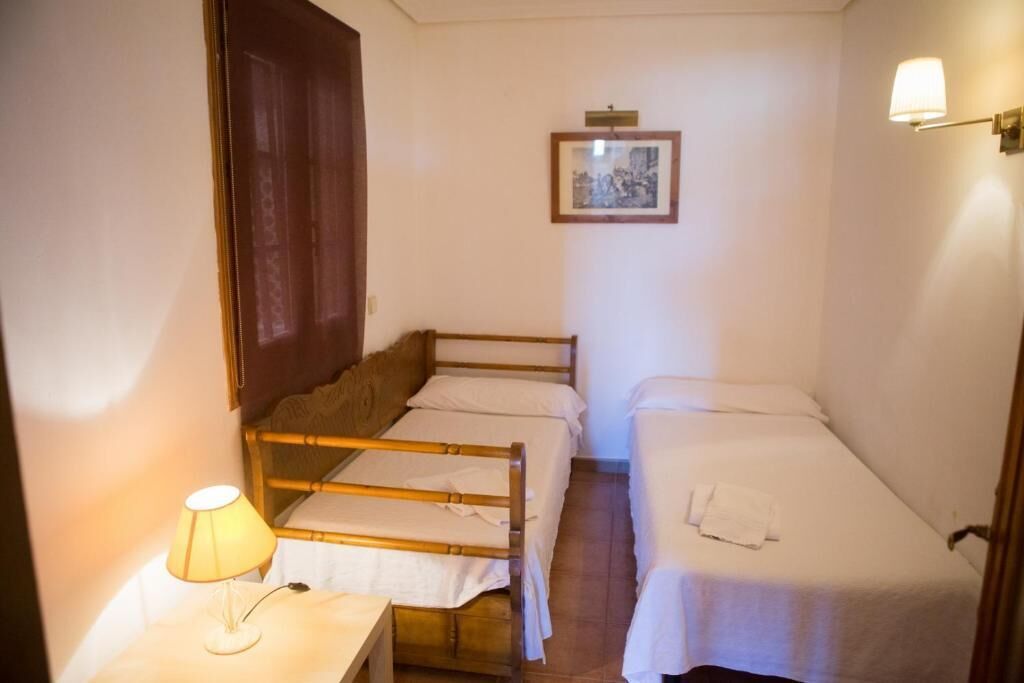 A small, compact room with two single beds, a bedside table with a lamp, and a framed picture on the wall.