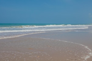 Une plage où les vagues viennent doucement lécher le rivage, un ciel dégagé et une mer calme.