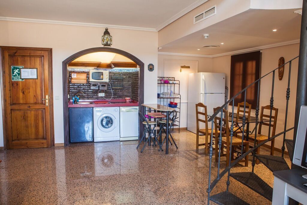 Angolo cottura compatto con lavatrice, forno a microonde e frigorifero. C'è una zona pranzo con tavolo e sedie, e una scala che conduce a un altro livello.