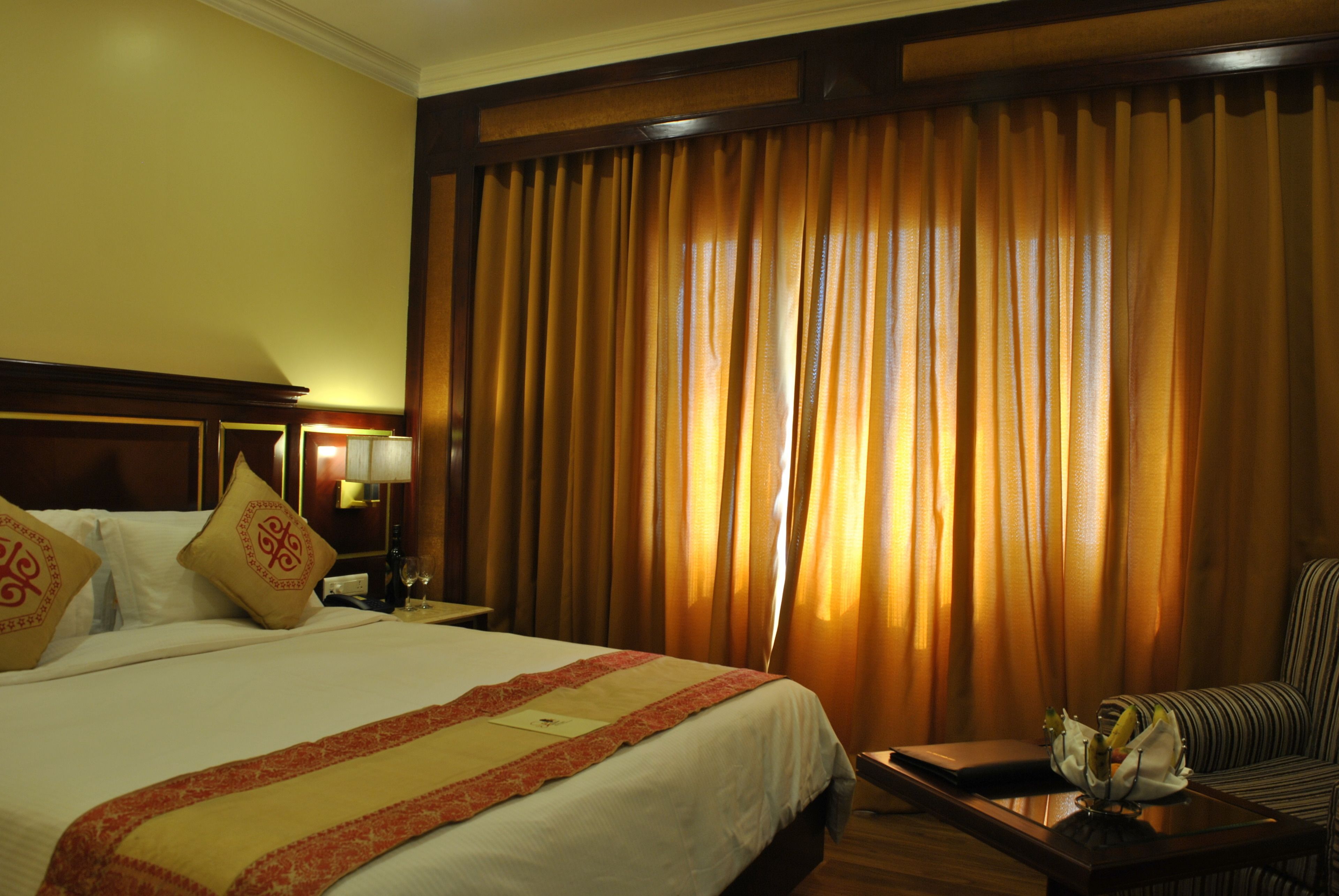 A hotel room with a large bed, a nightstand with a lamp, a sofa, and a window with curtains.