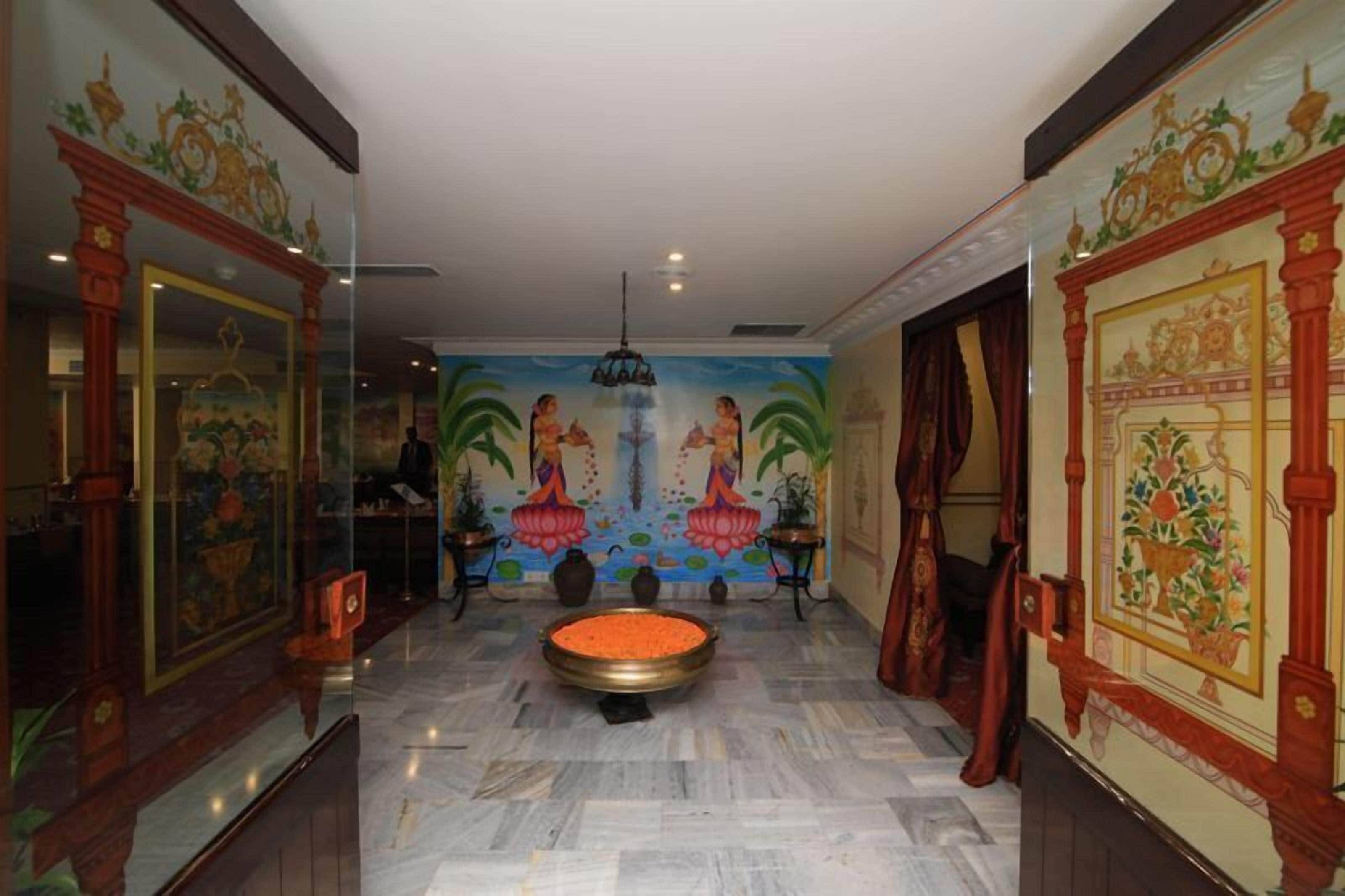 Un pasillo con una mesa redonda en el centro, flanqueado por decoraciones ornamentales en las paredes y un mural que muestra figuras con vestimenta tradicional.