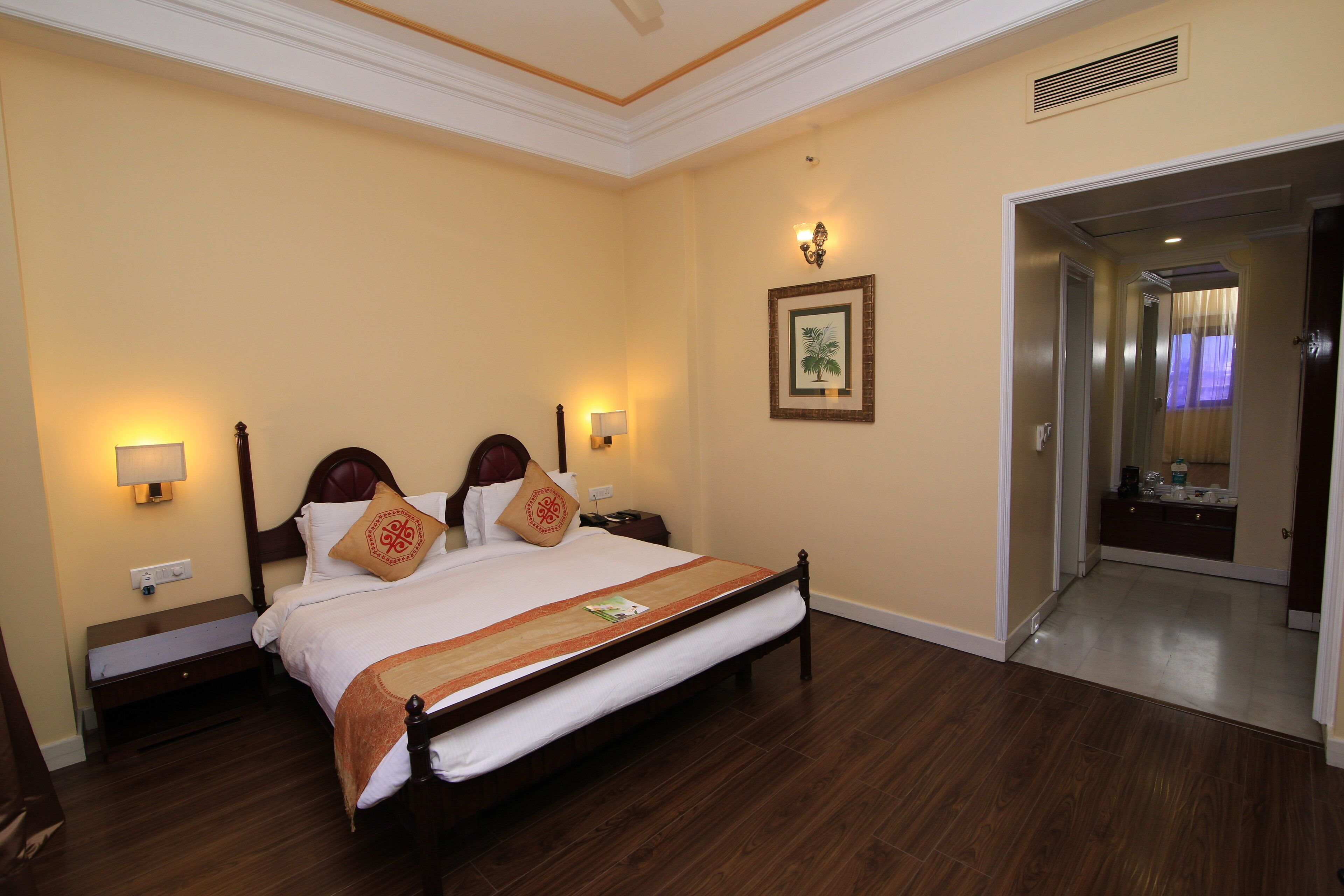 Habitación de hotel con una cama grande, lámparas de noche, un cuadro enmarcado en la pared y una puerta que da a otra habitación.