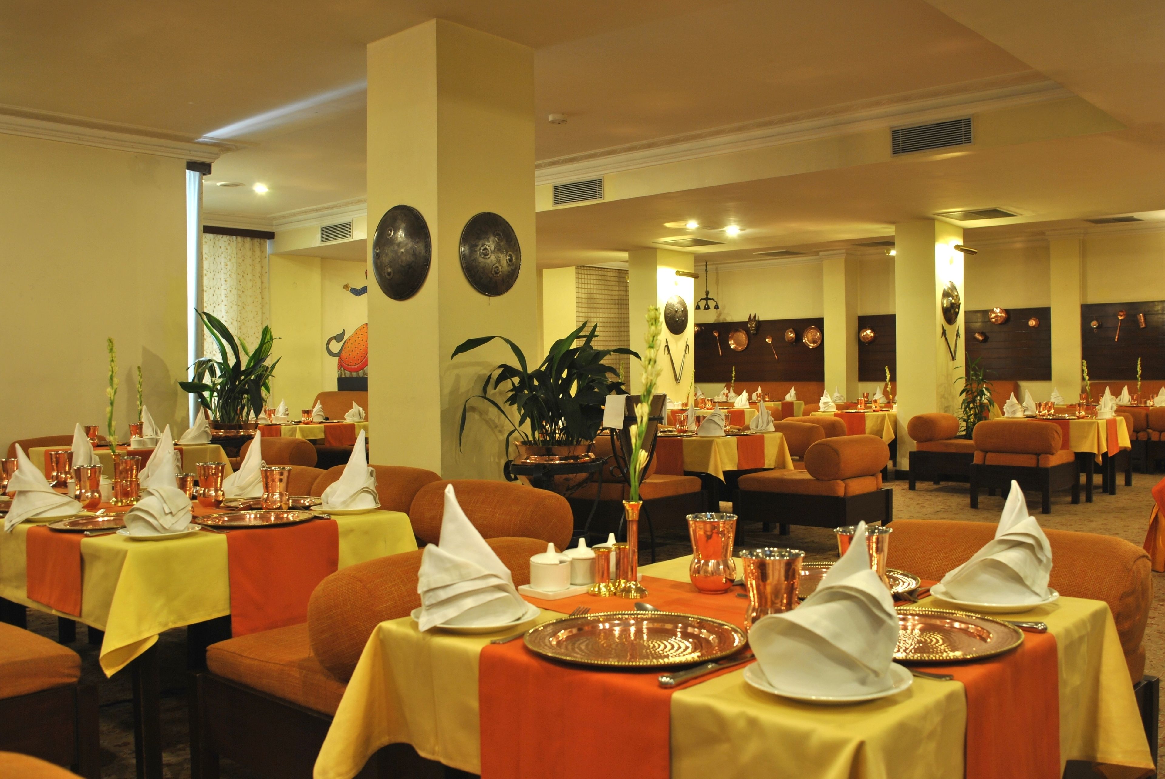 Un restaurant amb diverses taules preparades per dinar, amb camases ateses de taronja i groc, i diferents elements de taula com plats, gots i serrarecords.