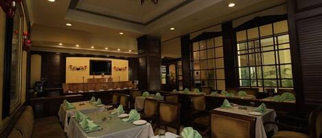Un restaurant avec plusieurs tables dressées pour le service, un coin bar et un écran de télévision.