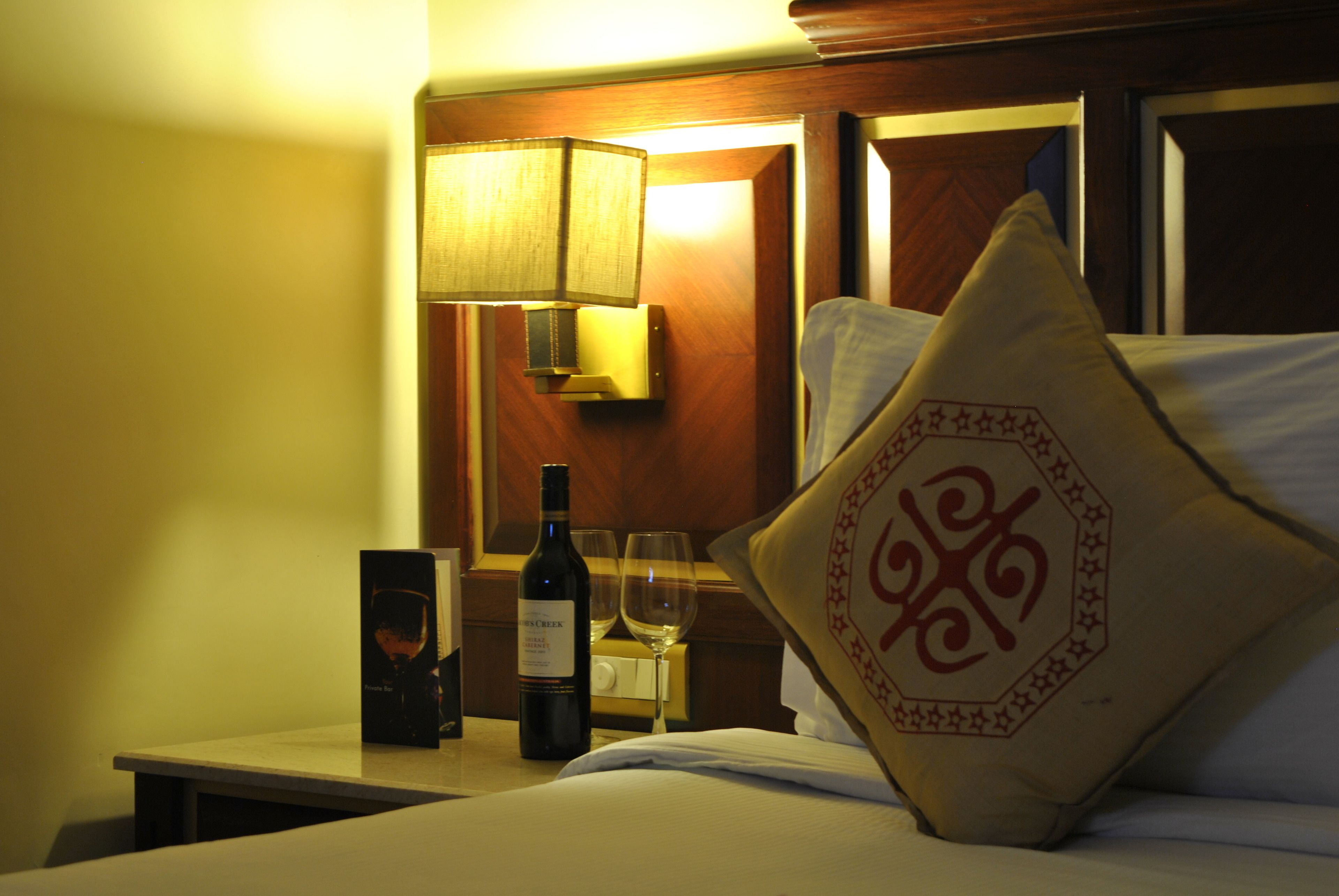 Een hotelkamer met een bed, nachtkastje, fles wijn en een glas.