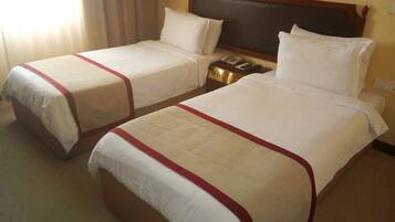 A hotel room with two single beds, each with a red-striped bedspread and white pillows. There is a wooden headboard, a bedside table with a lamp, and a telephone.