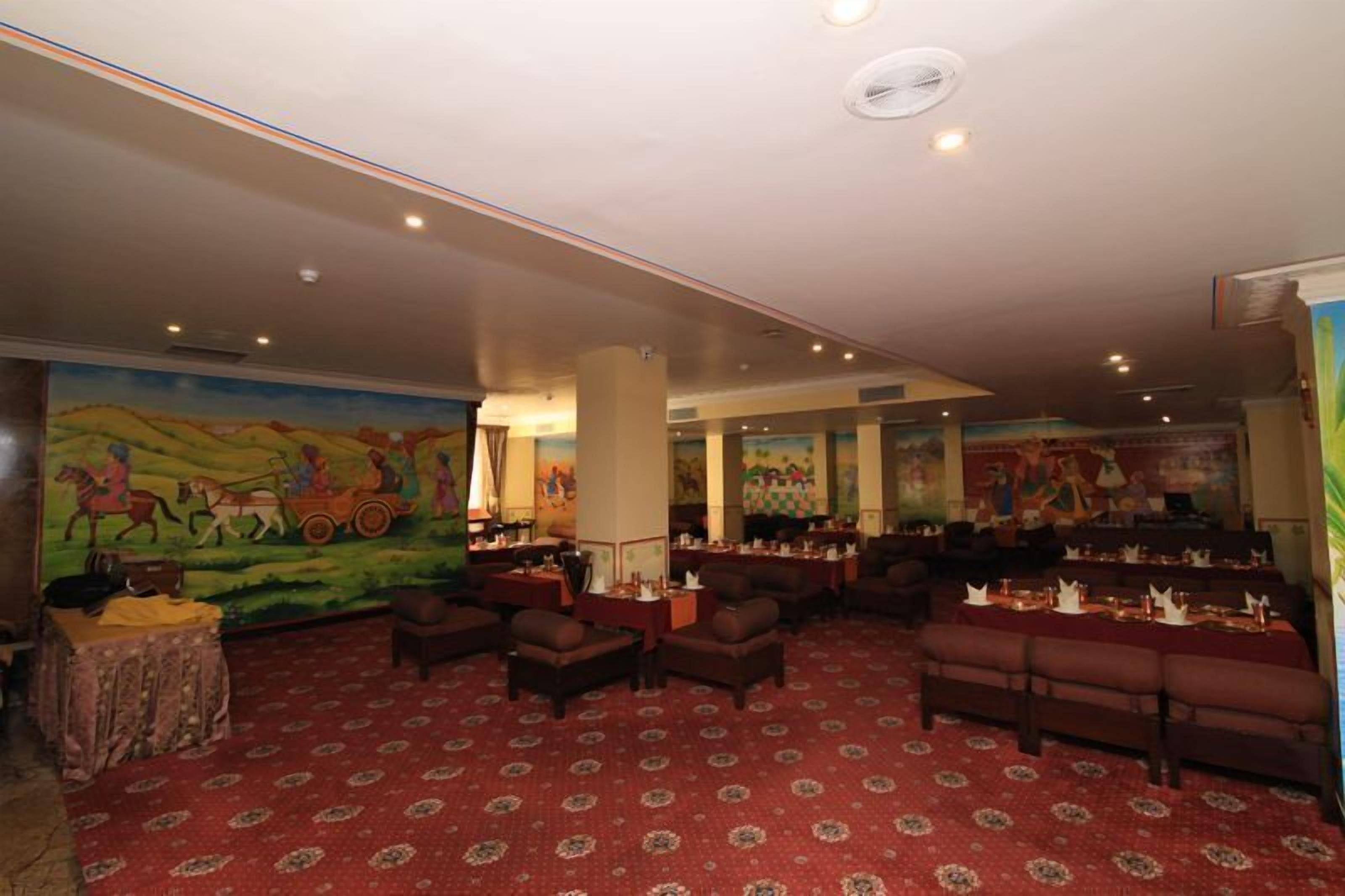 A spacious room with a red patterned carpet, multiple seating areas, and a mural depicting a historical scene on the wall.