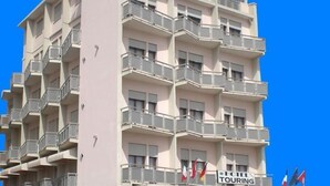 A multi-story hotel with balconies, a sign indicating hotel touring, and flags. - Hotel Touring (Chioggia)