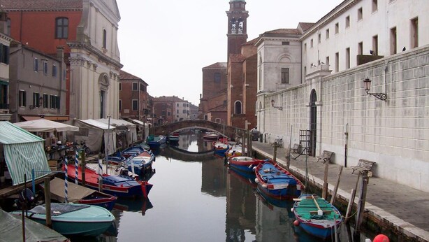 A canal with boats docked, historic buildings, and a clock tower. - Hotel Touring (Chioggia)