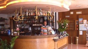 A bar area with a curved counter, a bartender, and shelves stocked with bottles. - Hotel Touring (Chioggia)