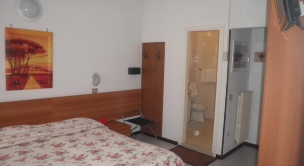 Un dormitorio con una cama, un escritorio pequeño, una puerta que da al baño y un cuadro en la pared.