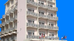 A multi-story hotel with balconies, a sign indicating it is a hotel and tour operator, and outdoor seating. - Hotel Touring (Chioggia)