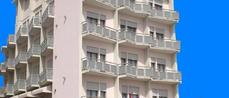 A multi-story hotel with balconies, a sign indicating it is a hotel and tour operator, and outdoor seating.