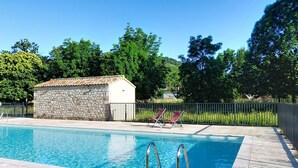 Una piscina con un edificio de piedra y dos sillas de descanso.