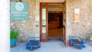 Entrada de un edificio de piedra con un cartel que indica 'Terres de France Domaine des Vans' y un mostrador de recepción en el interior.