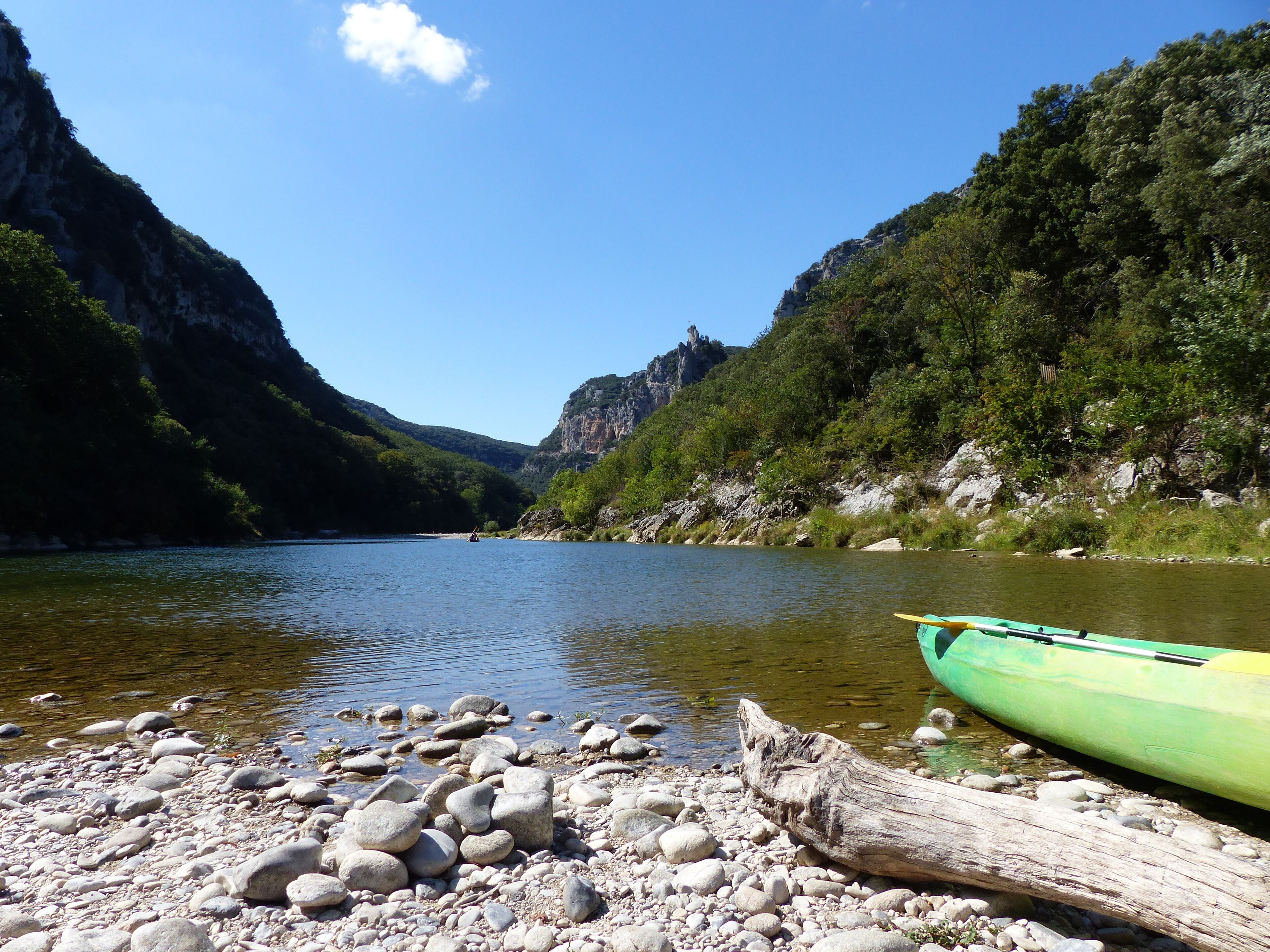 A calm river with a green kayak on the shore, surrounded by rocky terrain and dense greenery.