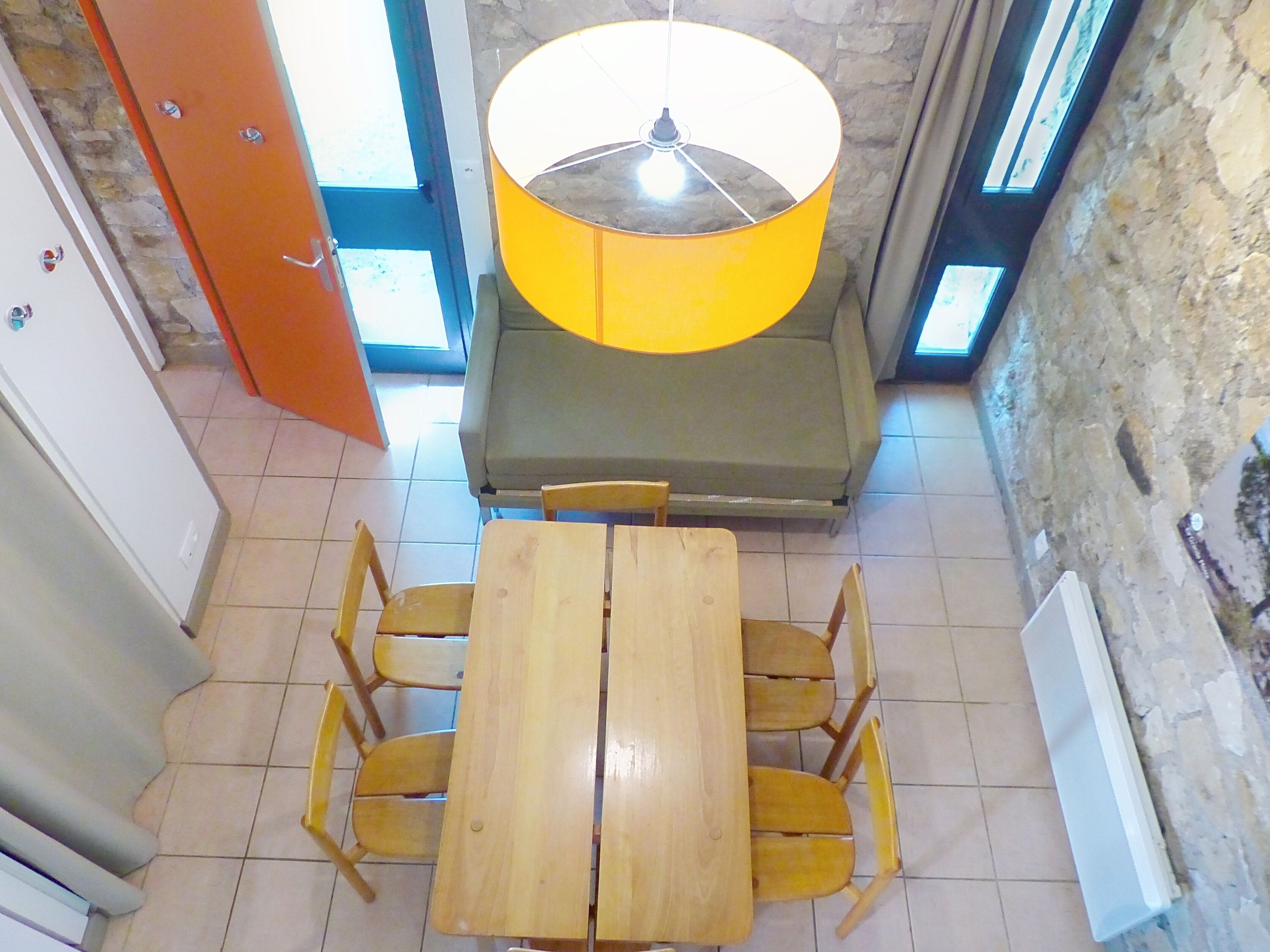 Ein Essbereich mit einem Holztisch und Stühlen, einer gelben Lampe und einer Steinsäule.