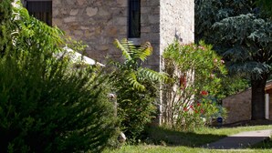 Un edificio de piedra con techo inclinado, rodeado de abundante vegetación y árboles altos.