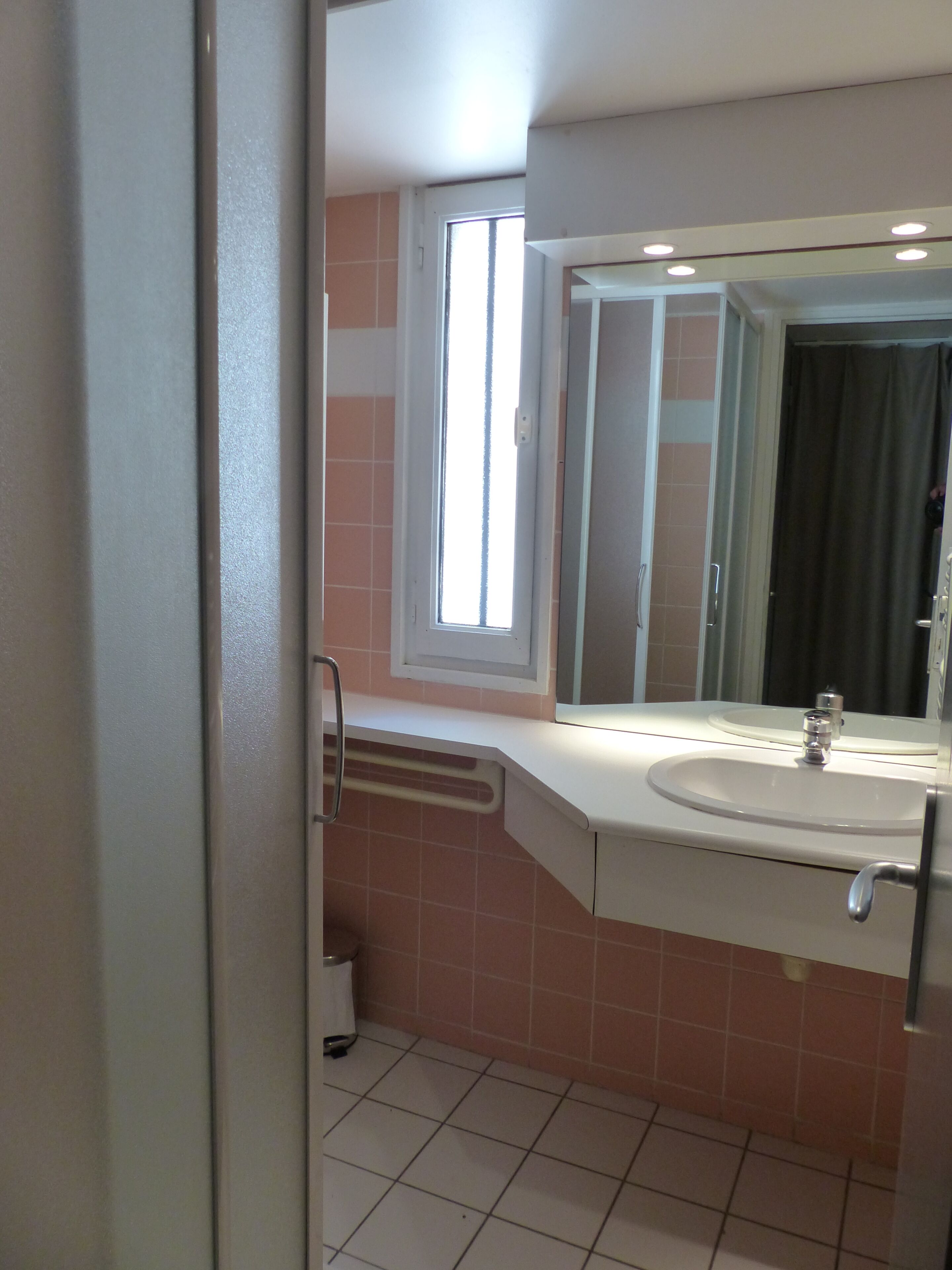 Ein Badezimmer mit Waschbecken, Spiegel, Fenster und Fliesenboden.