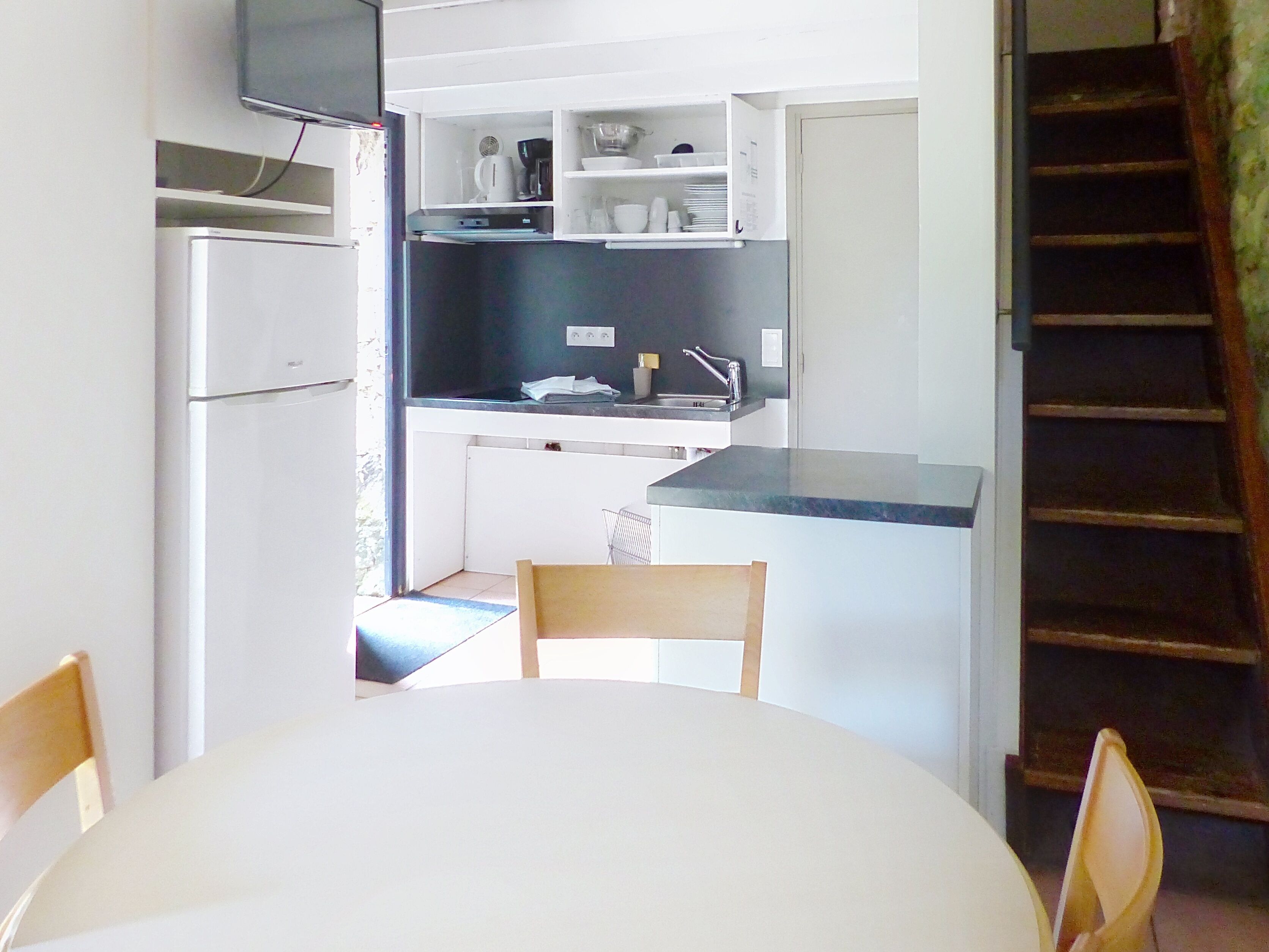 A compact kitchen with a dining table, chairs, a refrigerator, and a built-in oven.