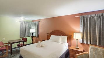 Quarto de hotel com cama, escrivaninha, cadeira, mesa de cabeceira e cortinas.