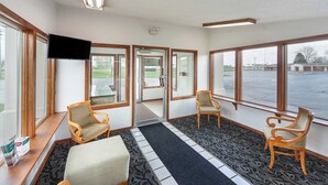A lobby with four wooden chairs, a flat-screen TV, and large windows offering a view of a parking lot.